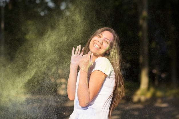 Affascinante donna asiatica abbronzata vestita con una camicia bianca, che gioca con la polvere di Holi nel parco