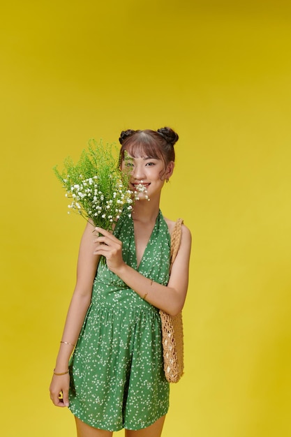 Affascinante donna asiatica in tuta estiva verde con fiori di campo nelle sue mani sorridenti