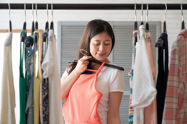 affascinante donna asiatica nel guardaroba con un vestito nuovo che sorride provando. gioiosa bella ragazza coreana che raccoglie vestito al mattino in camera da letto. allegro cinese femminile amore moda stile di vita panno.