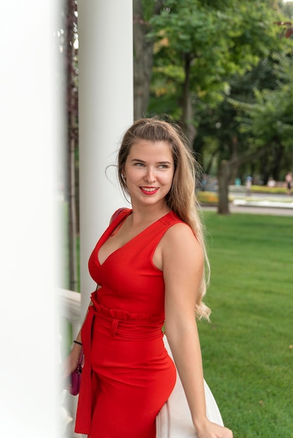 Affascinante donna bionda in abito rosso con profonda scollatura Ritratto di giovane donna sexy nel parco estivo