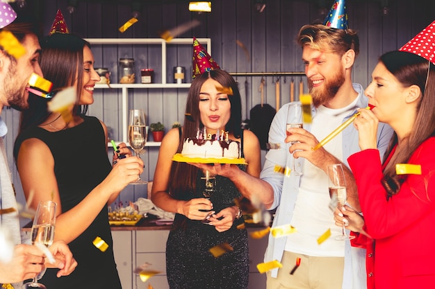 Affascinante donna che soffia sulle candele sulla torta di compleanno dopo aver espresso il suo desiderio alla festa