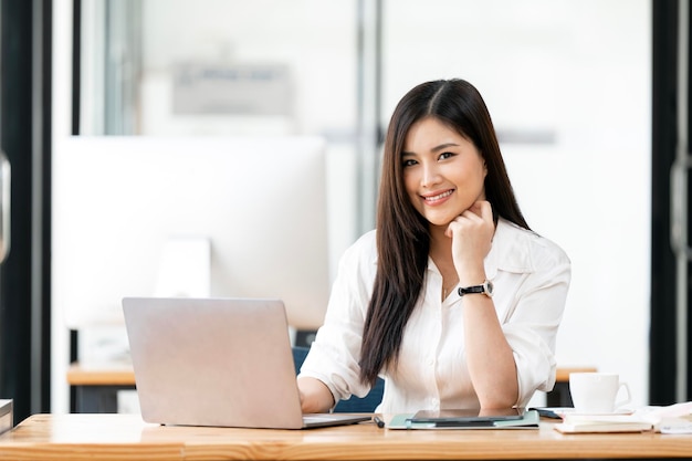 Affascinante donna d'affari asiatica seduta a lavorare al portatile in ufficio