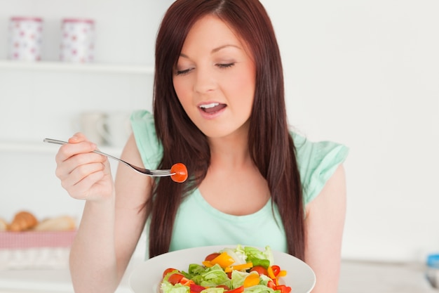 Affascinante donna dai capelli rossi che gode di un&#39;insalata mista in cucina