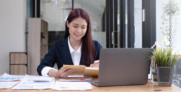 Affascinante donna di affari asiatica che si siede lavorando sul computer portatile in ufficio