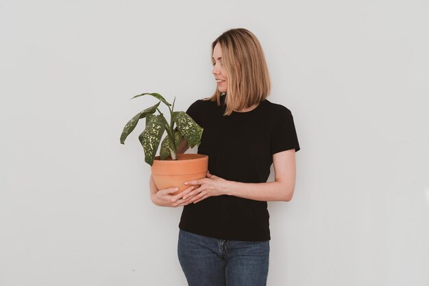 Affascinante donna europea in abiti casual che tiene la pianta domestica in vaso