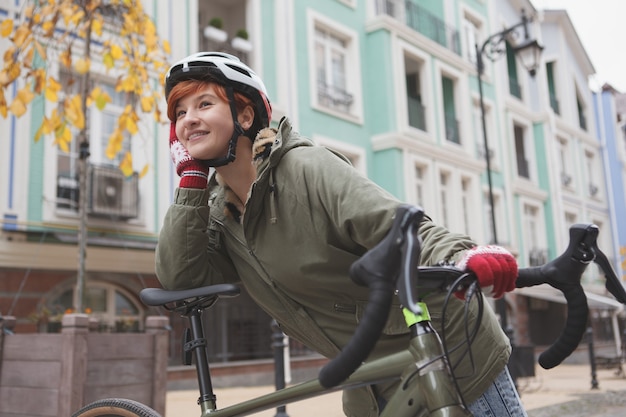 Affascinante donna felice che indossa il casco protettivo in bicicletta, appoggiato sulla sua bicicletta durante il riposo