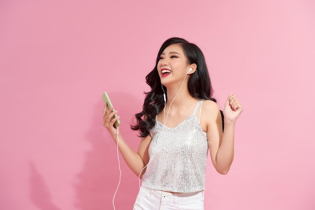 affascinante donna gioiosa che sorride dalla gioia che ascolta musica in auricolari che tengono smartphone