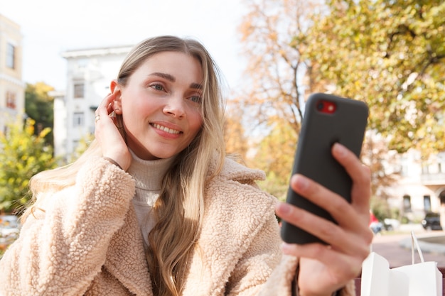 Affascinante donna sorridente, prendendo selfie con il suo smartphone all'aperto in una soleggiata giornata autunnale