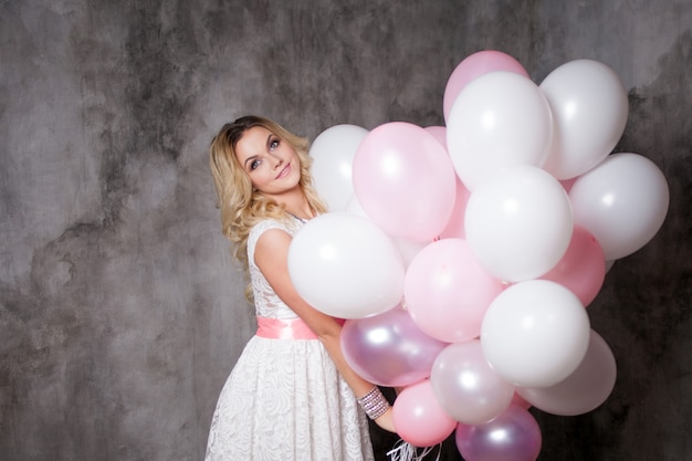 Affascinante giovane bionda in abito bianco con palloncini rosa, alla festa.