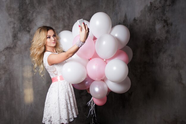 Affascinante giovane bionda in un abito bianco con palloncini rosa, fare un selfie