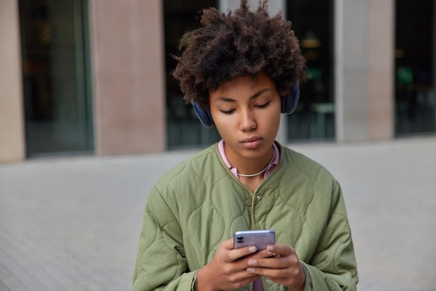 Affascinante giovane donna ascolta podcast musicali durante il tempo libero utilizza l'applicazione per l'ascolto di brani audio tiene il telefono cellulare