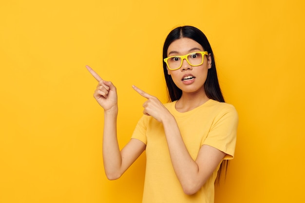 Affascinante giovane donna asiatica con gli occhiali che gesturing con le mani copyspace sfondo giallo inalterato