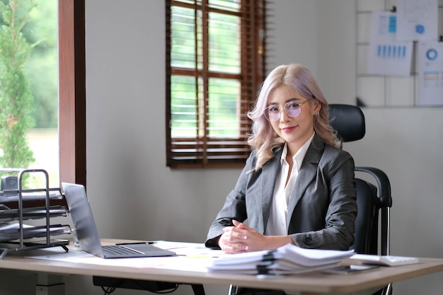 Affascinante giovane donna asiatica con gli occhiali in possesso di un portatile penna notebook in ufficio Guardando la telecamera