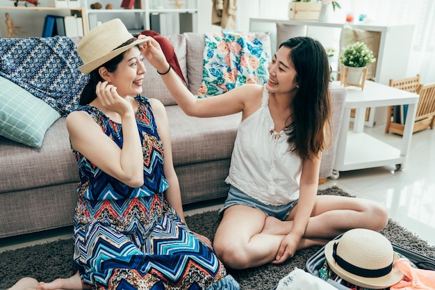 Affascinante giovane donna che prova il cappello di paglia che sorride all'amico chiedendo un parere mentre prepara i bagagli per le vacanze estive negli Stati Uniti. le ragazze impediscono il concetto di stile di vita di protezione solare solare. momenti reali