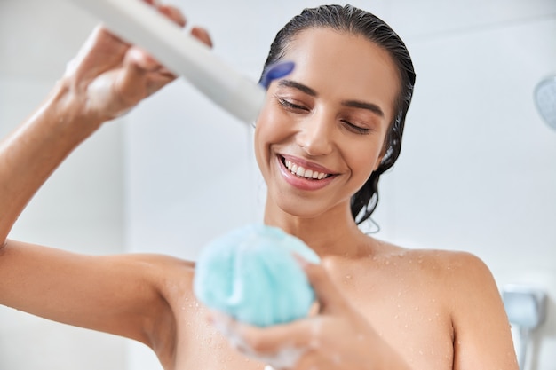 Affascinante giovane donna che versa gel doccia sulla luffa da bagno