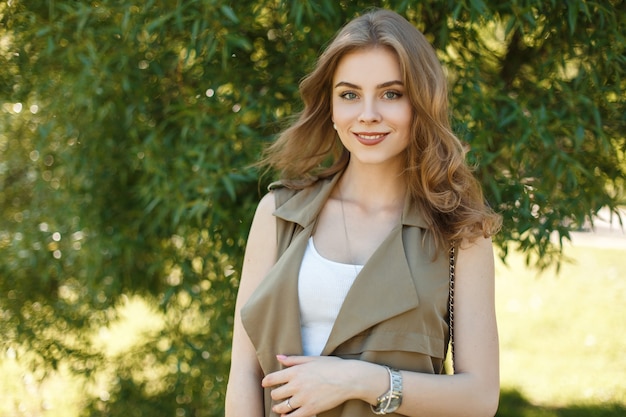 Affascinante giovane donna con un bel sorriso in un giubbotto estivo alla moda in una maglietta bianca è in piedi