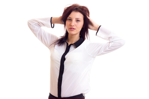 Affascinante giovane donna in camicia bianca e pantaloni neri con capelli scuri su sfondo bianco in studio