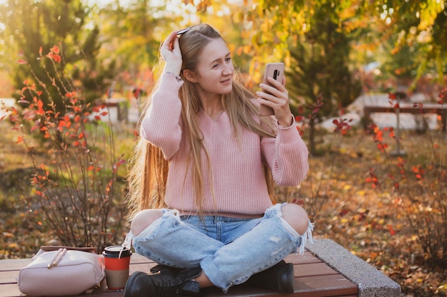 Affascinante giovane donna in stile casual comunica al telefono mentre è seduto su una panchina nel parco