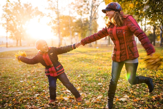 Affascinante giovane madre e figlia che ballano mentre camminano in un caldo parco autunnale