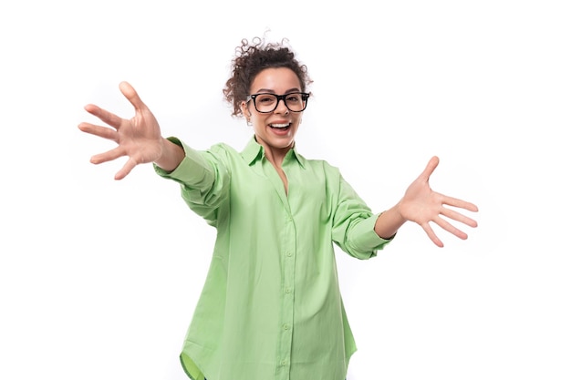 Affascinante giovane modello femminile sottile vestita con una camicia verde chiaro agitando le mani su un bianco