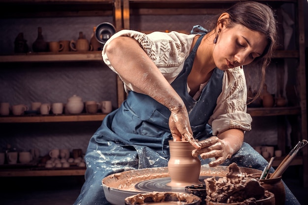 Affascinante maestro scultore artigiano lavora con l'argilla su un tornio da vasaio ea tavola con gli strumenti. Produzione artigianale.