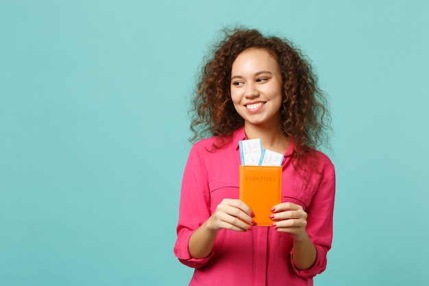 Affascinante ragazza africana in abiti casual rosa in possesso di passaporto, biglietto della carta d'imbarco isolato su sfondo blu turchese parete in studio. Concetto di stile di vita di emozioni sincere della gente. Mock up copia spazio.