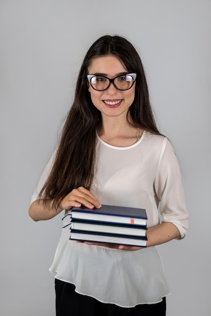 Affascinante ragazza insegnante che tiene il libro con gli occhiali e la camicia isolati su un certo sfondo