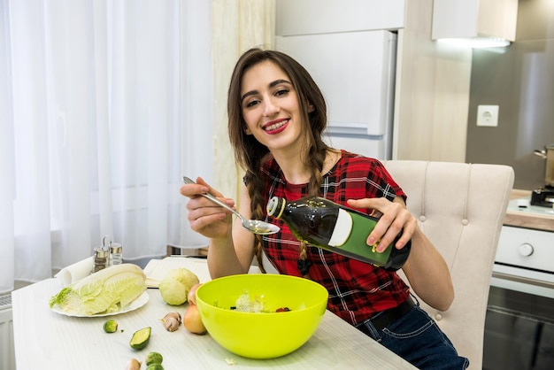 Affascinante ragazza prepara un'insalata di diverse verdure e verdure aromatizzate con olio d'oliva per uno stile di vita sano