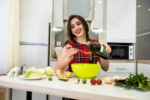 Affascinante ragazza prepara un'insalata di diverse verdure e verdure aromatizzate con olio d'oliva per uno stile di vita sano