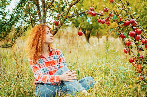 Affascinante ritratto di donna dai capelli rossi nel giardino delle mele sullo sfondo di ramoscelli con mele rosse