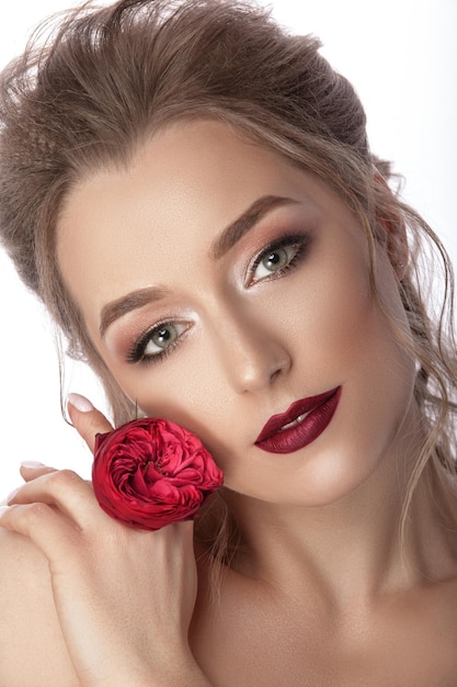 Affascinante ritratto dolce di una giovane ragazza con un fiore rosso nelle sue mani Bellissimo trucco e acconciatura Sfondo bianco isolato fotografato