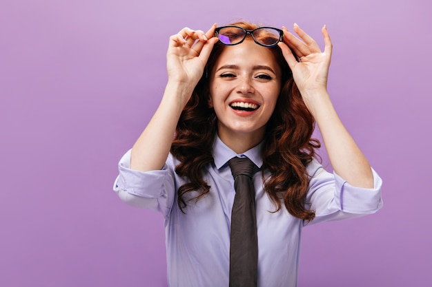 Affascinante signora in camicia blu che si toglie gli occhiali e ride