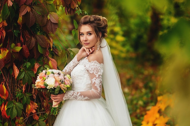 Affascinante sposa con bouquet di fiori si trova in una foresta mistica