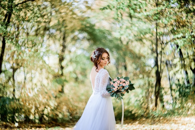 Affascinante sposa con fiori beige nei suoi amrs si erge sul tappeto di foglie cadute