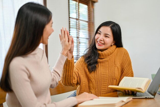 Affascinante studentessa universitaria asiatica che dà il cinque alla sua migliore amica mentre fa i compiti