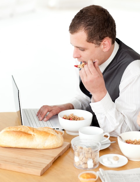 Affascinante uomo d&#39;affari utilizzando un computer portatile pur avendo la colazione