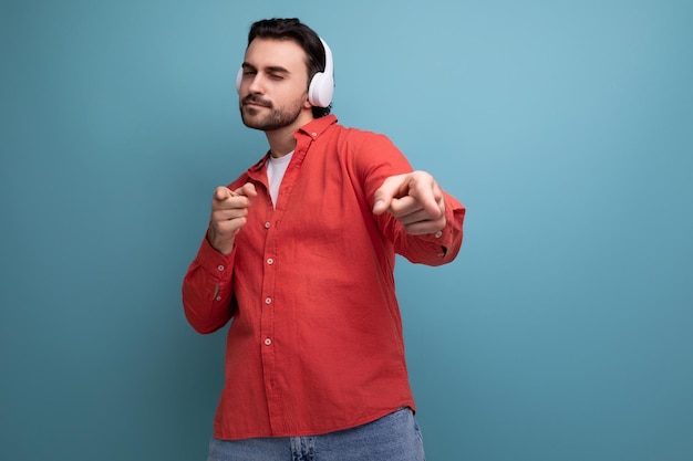 Affascinante uomo positivo in camicia rossa con cuffie bianche wireless