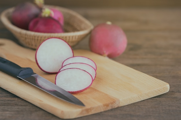 Affetta il ravanello rosso fresco dal coltello da cucina e dal tagliere di legno sulla tavola di legno.