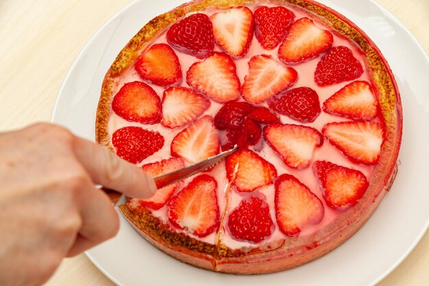 Affettare a mano la migliore crostata di fragole fatta in casa isolata su sfondo di legno Vista dall'alto