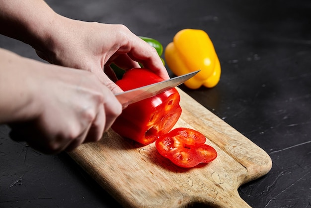 Affettare il pepe Coltello per le mani e peperoni gialli verdi rossi tagliere in legno insalata cibo sano