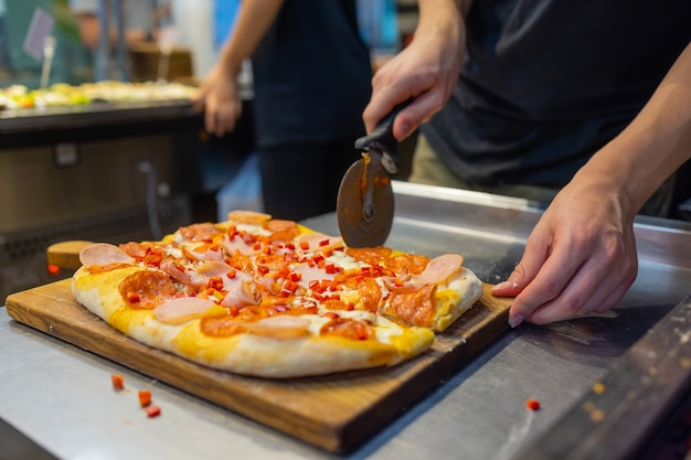 Affettare la pizza finita con mani maschili con un coltello