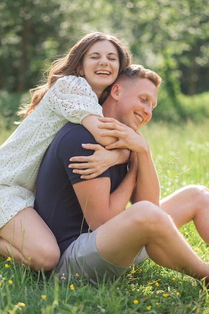 Affettuosa giovane coppia seduta sull'erba nel parco che abbraccia il giovane e la donna che si godono la giornata estiva