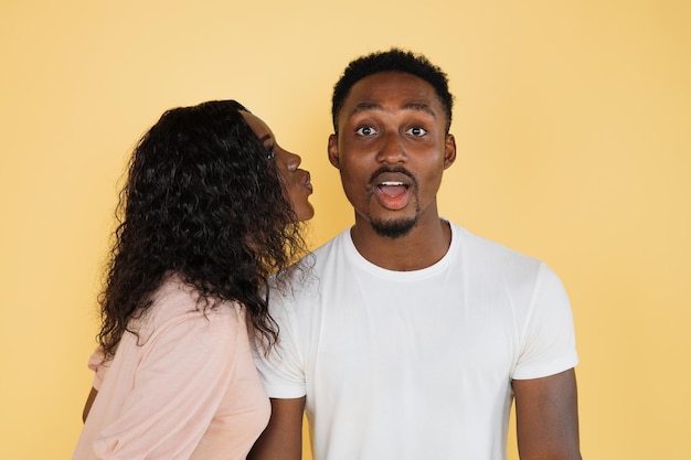 Affettuose giovani donne africane provano a baciare il suo fidanzato eccitato su sfondo giallo studio