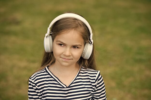 Affronta la musica La bambina ascolta la musica all'aperto Il bambino piccolo indossa le cuffie mentre suona musica Nuova tecnologia Vita moderna Vacanze estive Divertimento e intrattenimento Ascoltalo