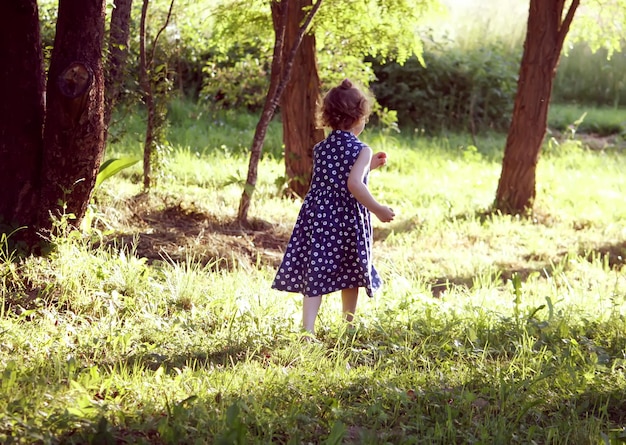 Aforabile bambina con i capelli ricci che cammina nel giardino estivo in campagna