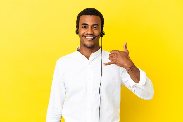 African American Telemarketer uomo che lavora con un auricolare su sfondo giallo isolato che fa il gesto del telefono. Richiamami segno