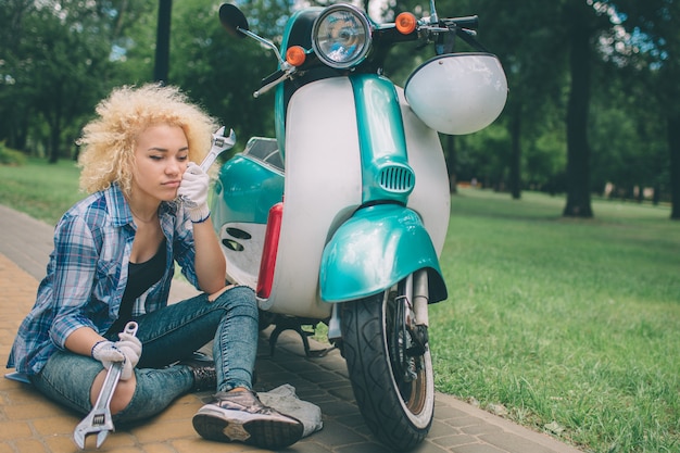 Afro-americana, signora giovane riparazione di uno scooter sulla strada Mulatta femmina nera nel parco