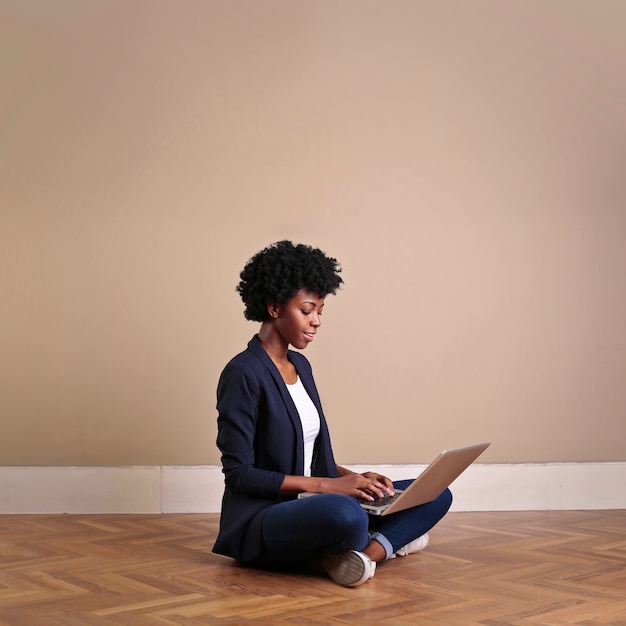 Afro donna seduta sul pavimento con un computer portatile