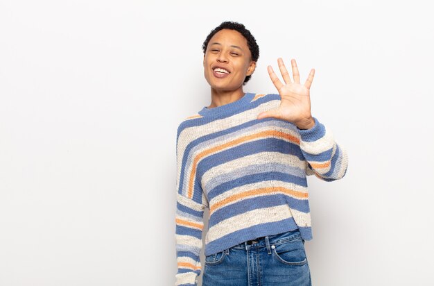 afro giovane donna nera sorridente e guardando amichevole, mostrando il numero cinque o quinto con la mano in avanti, il conto alla rovescia