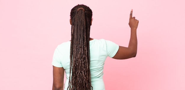 Afro nero adulto donna in piedi e puntando a un oggetto sullo spazio della copia, vista posteriore